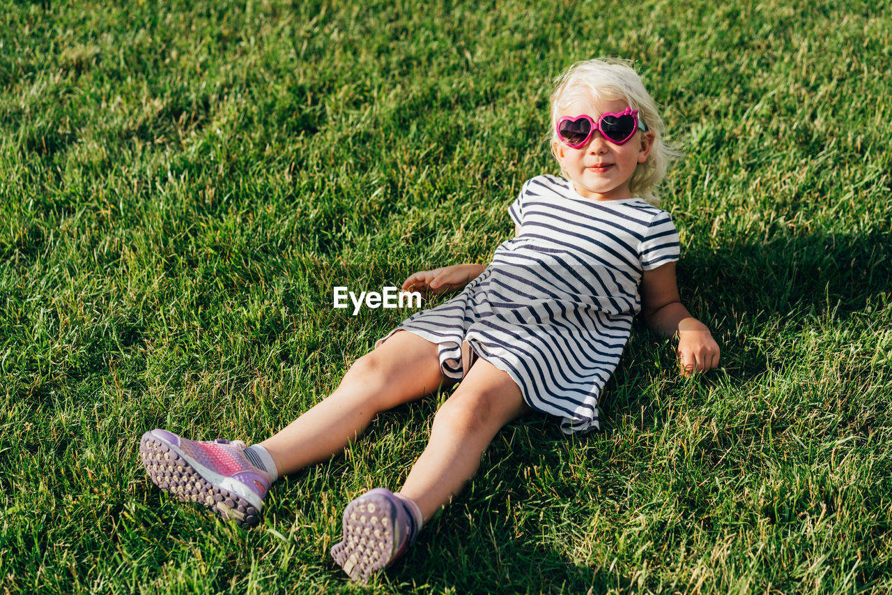 Little stylish girl in sunglasses lies on the lawn