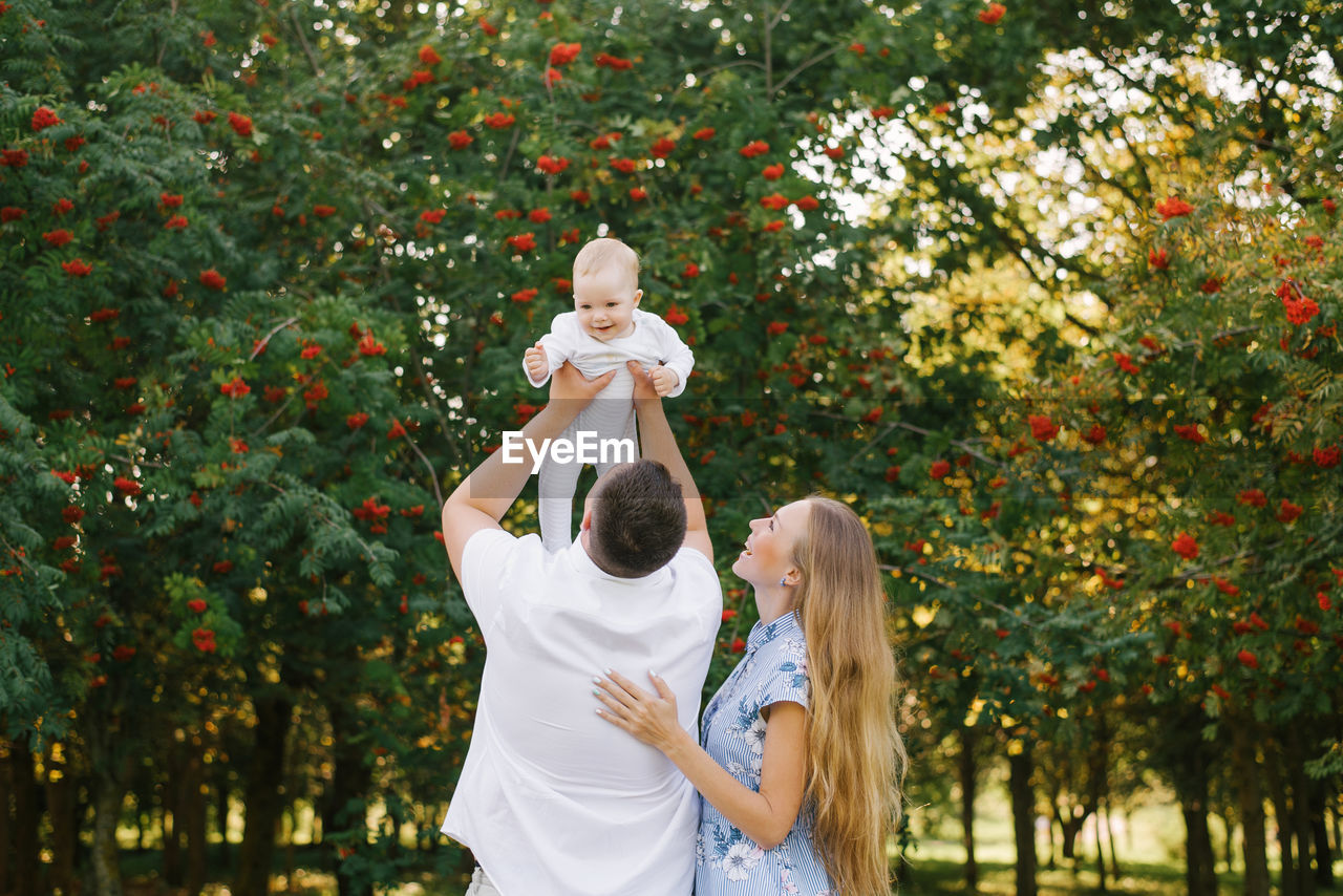 A father and mother play with their son in the park in the summer. a man holds a little boy up
