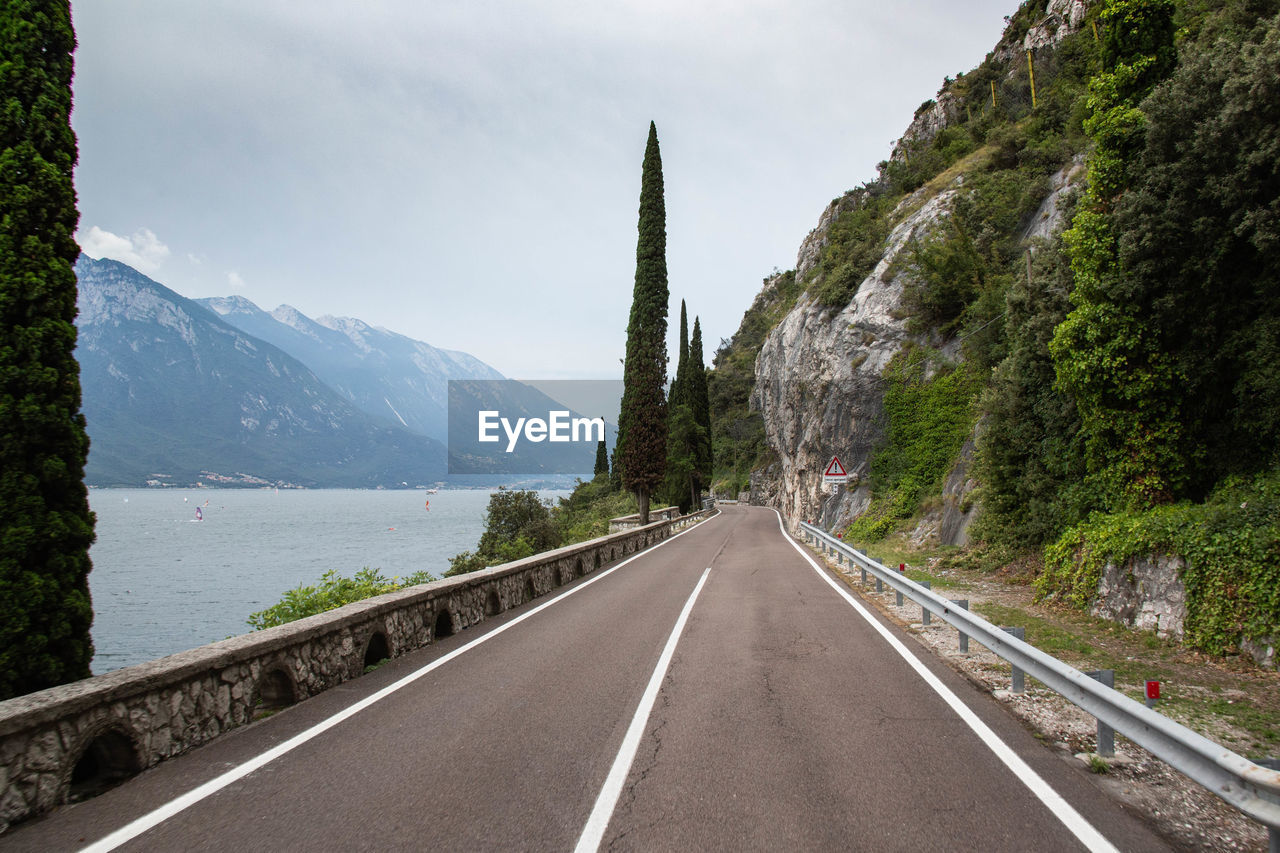 Empty road by mountains against sky at lake garda italy