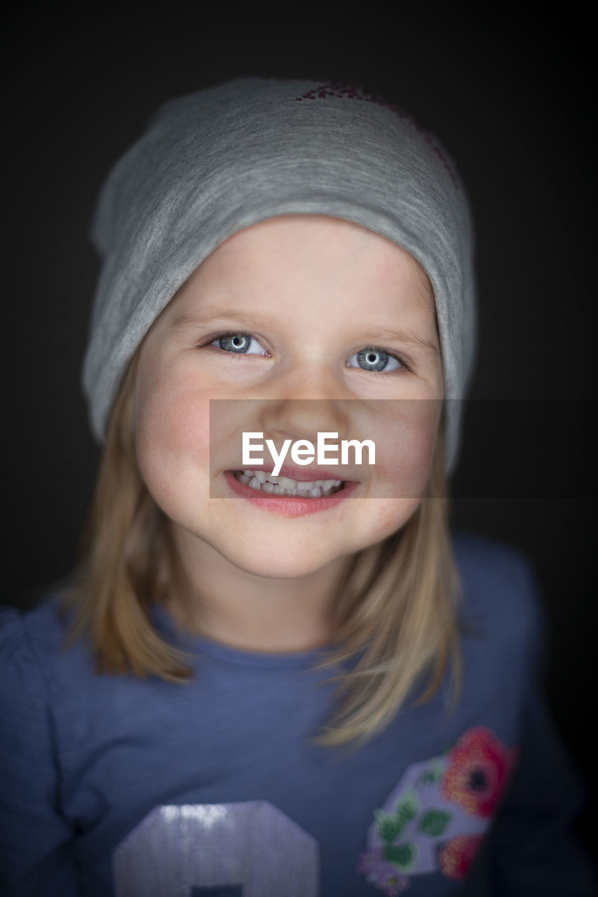 portrait, looking at camera, child, childhood, smiling, one person, front view, headshot, happiness, indoors, emotion, toddler, baby, skin, cap, blue, studio shot, human face, black background, close-up, women, clothing, portrait photography, innocence, person, female, blond hair, human head, hat, headgear, cheerful, cute, knit cap, casual clothing, white