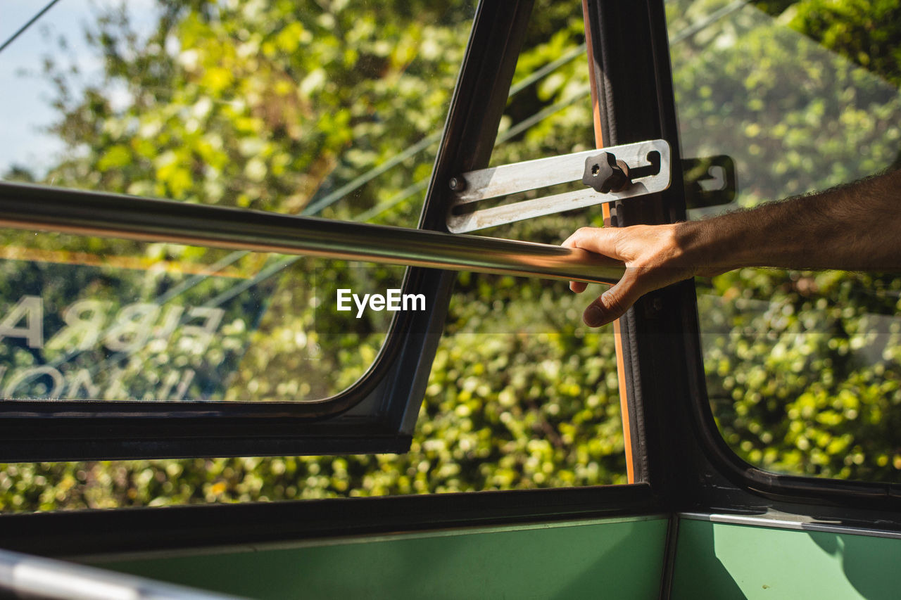 Cropped hand of man by window in bus