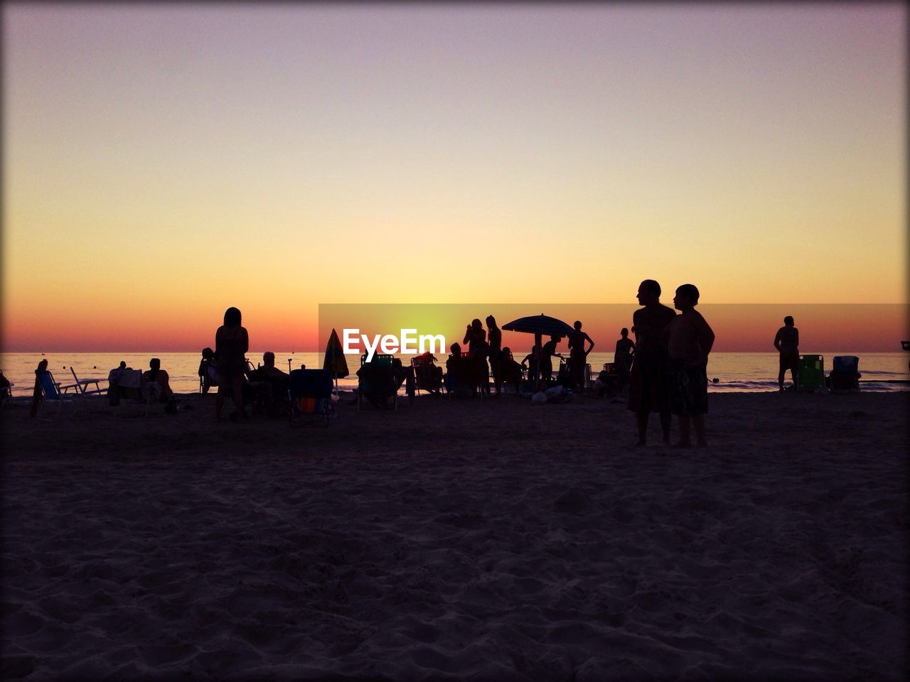 People enjoying at beach against sky during sunset