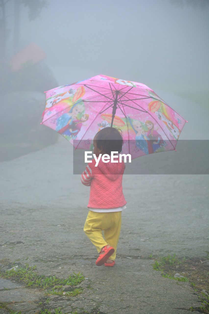 REAR VIEW OF BOY HOLDING UMBRELLA WALKING ON STREET