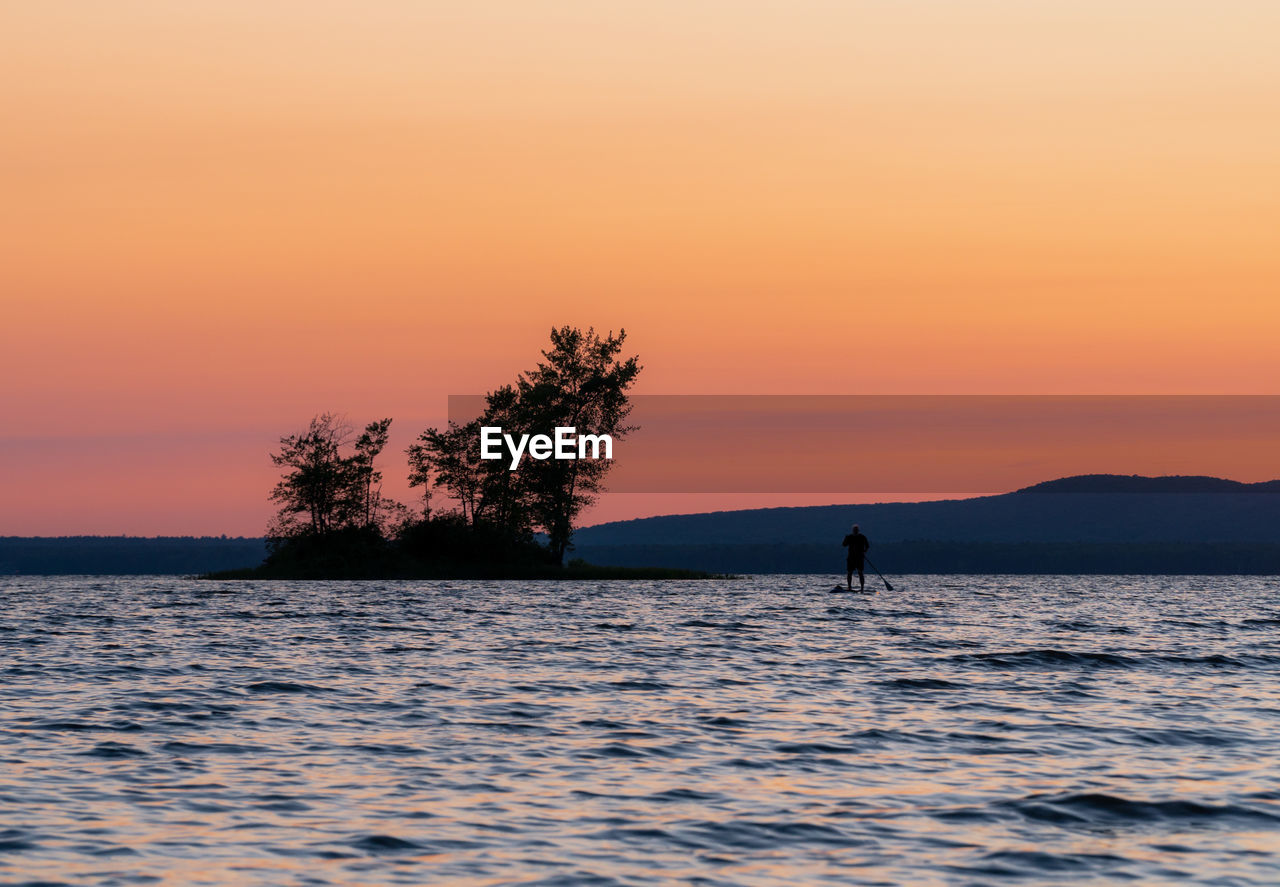 Silhouette person in sea against sky during sunset