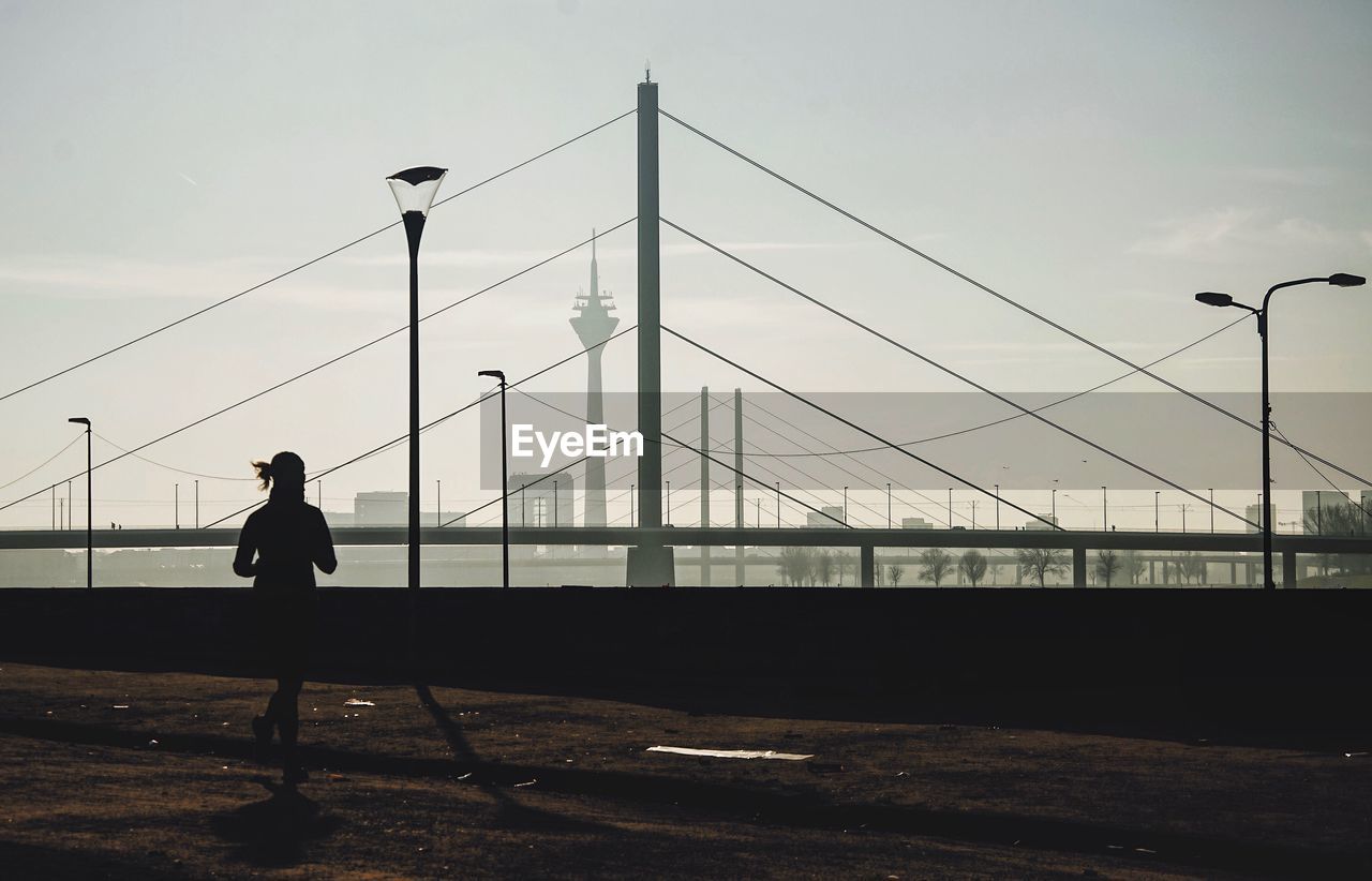 Silhouette man walking on footpath against sky in city