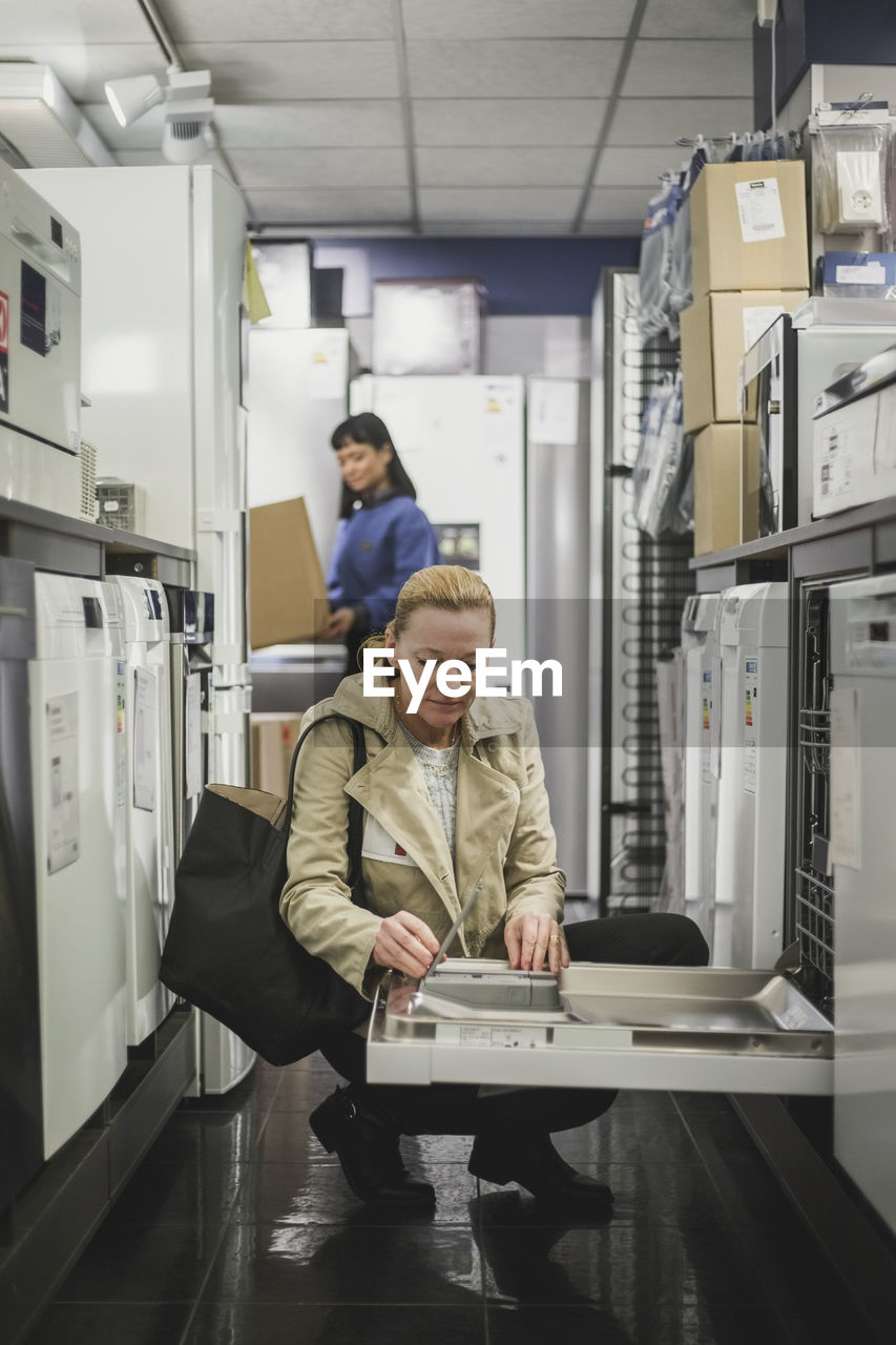 Mature customer looking at oven while crouching in electronics store