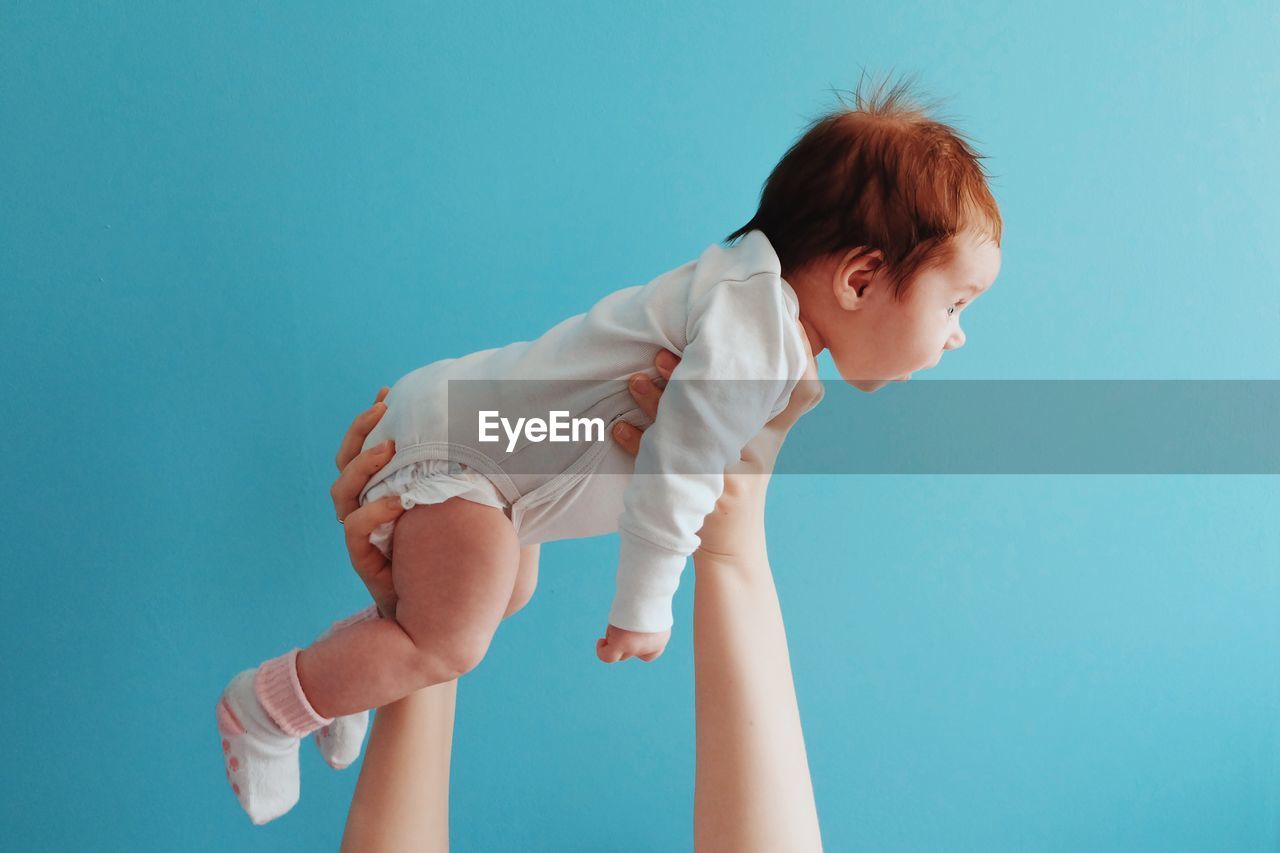 Cute baby rides in fathers hands against blue background