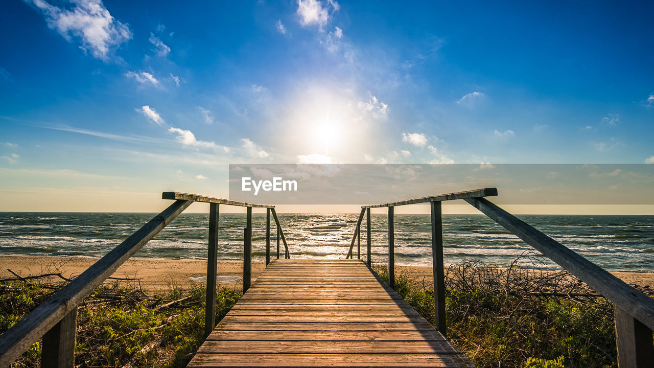 Boardwalk leading to sea against sky