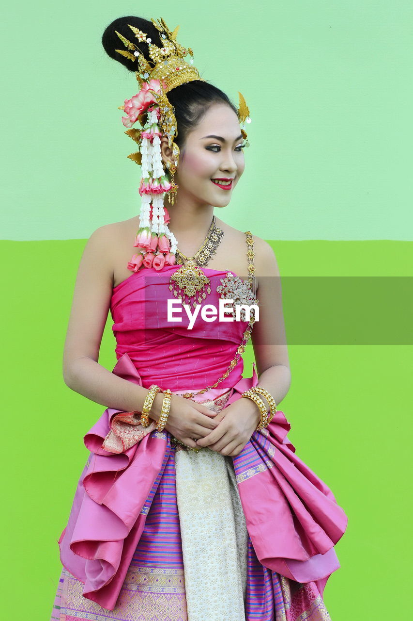 Smiling young woman wearing traditional clothing against wall