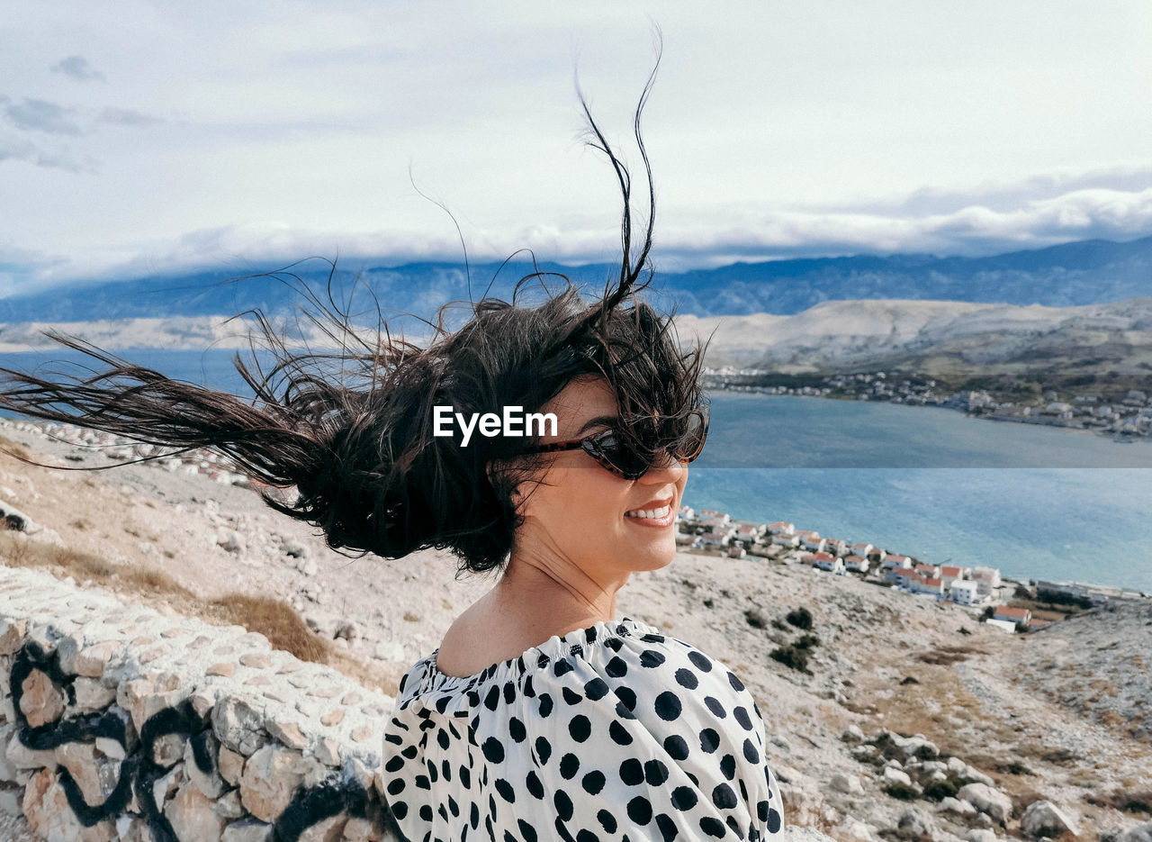 Rear view of young woman on viewpoint over sea. wind blowing hair.