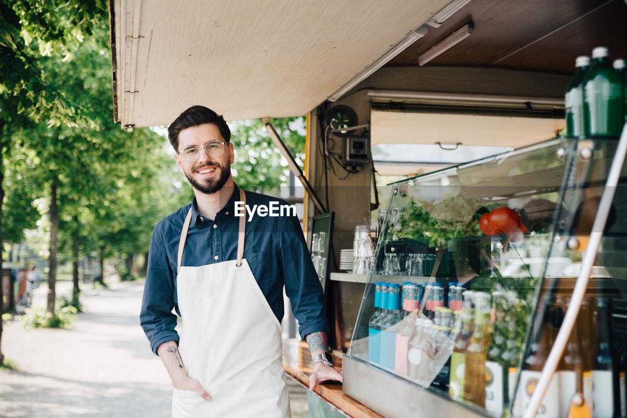 Portrait of young owner standing by commercial land vehicle on street