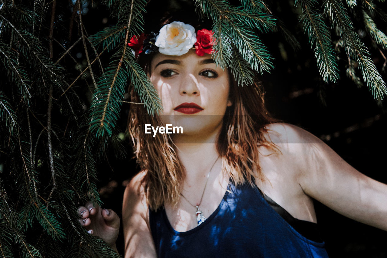 Beautiful young woman wearing flowers amidst branches