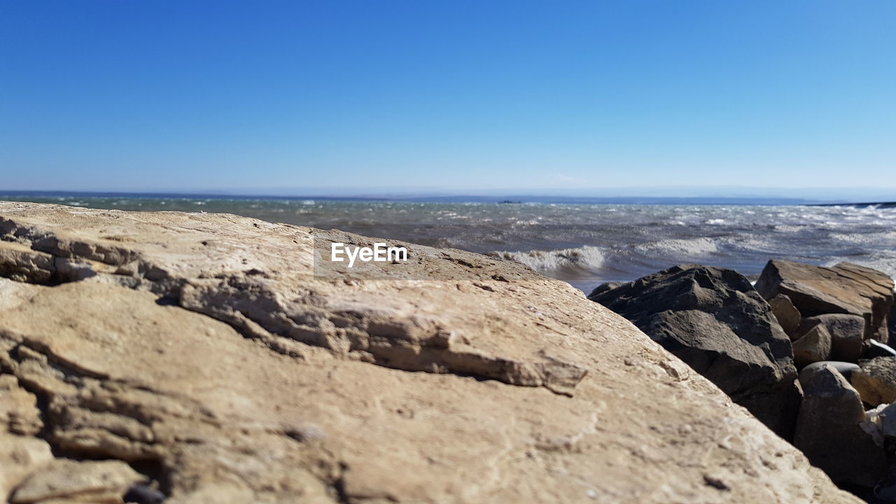 ROCKS ON BEACH AGAINST CLEAR BLUE SKY