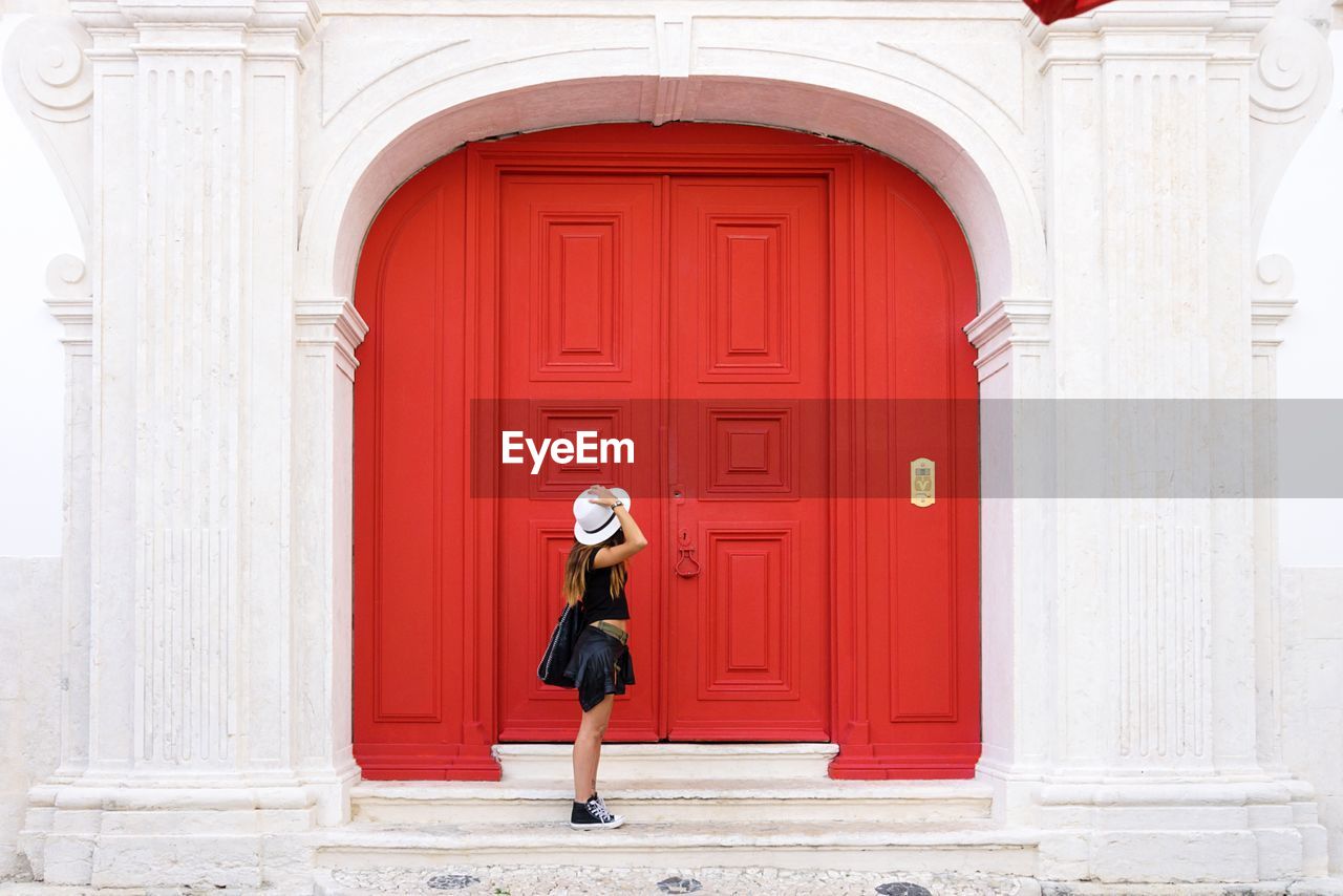 Side view of woman standing by closed red door
