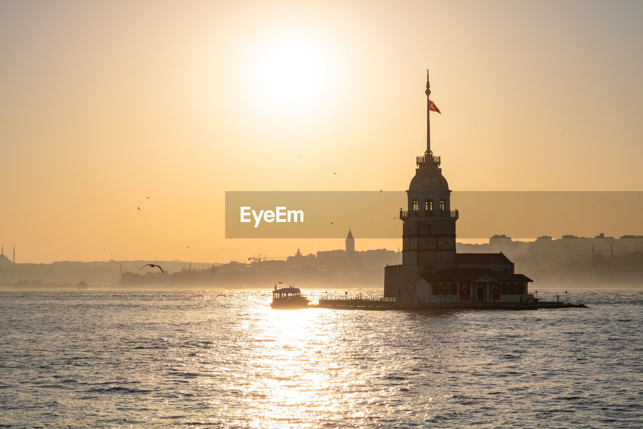 Lighthouse by sea against clear sky during sunset