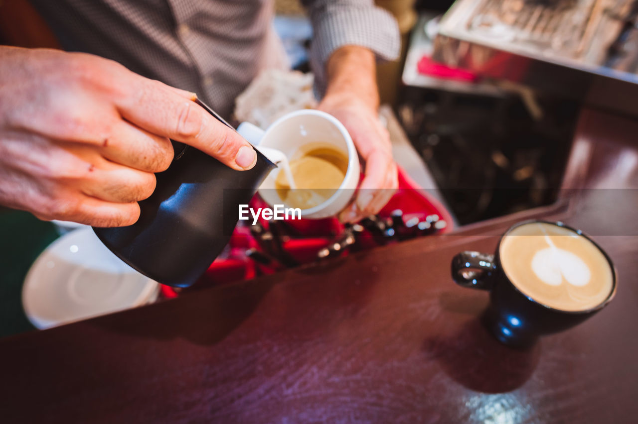 Midsection of barista pouring coffee in cup from container at cafe