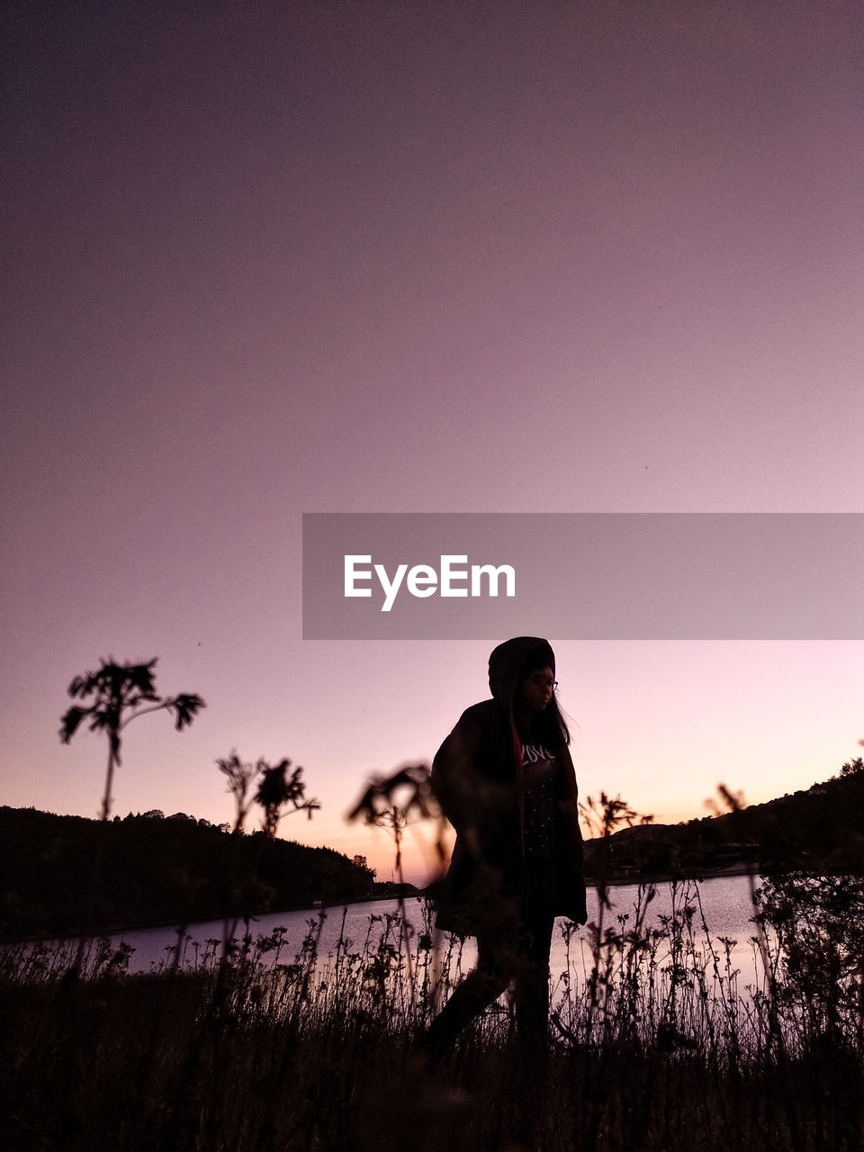 Silhouette teenage girl standing by lake against clear sky during sunset