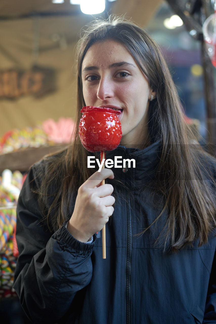Portrait of teenage girl having taffy apple in city