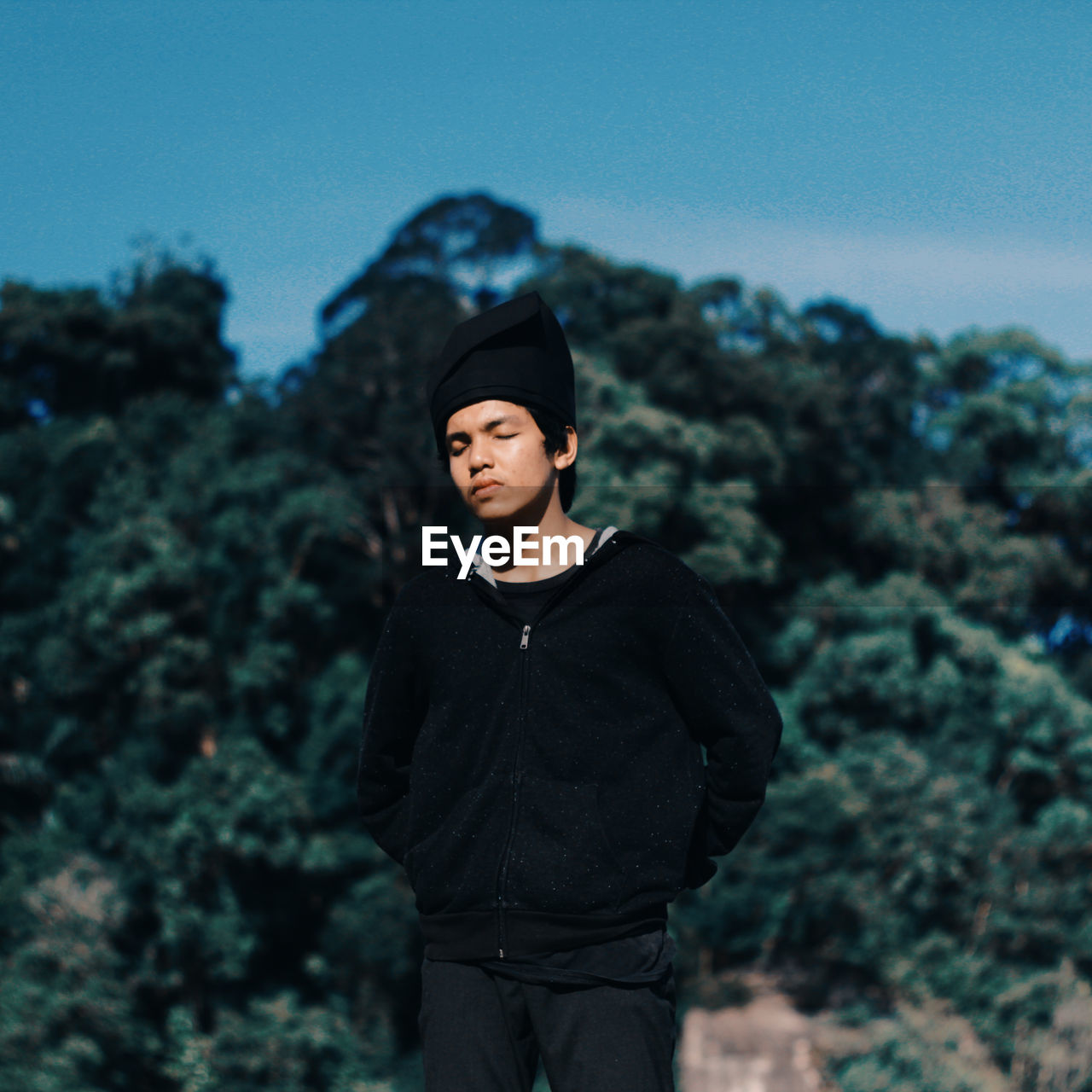 Teenage boy with eyes closed standing against trees