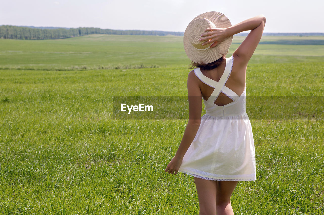 one person, meadow, grass, clothing, women, plant, sun hat, adult, nature, hat, field, landscape, land, grassland, dress, environment, fashion, summer, green, young adult, agriculture, standing, rear view, sky, leisure activity, day, plain, straw hat, rural scene, tranquility, female, hairstyle, beauty in nature, lawn, three quarter length, sunlight, outdoors, relaxation, long hair, vacation, lifestyles, person, trip, carefree, emotion, natural environment, copy space, holiday, happiness, full length, tranquil scene, enjoyment, fashion accessory, child, looking, sundress, limb, casual clothing, portrait, holding, scenics - nature, smiling, solitude, childhood, idyllic, non-urban scene, brown hair, travel, skirt, blond hair, positive emotion, arm