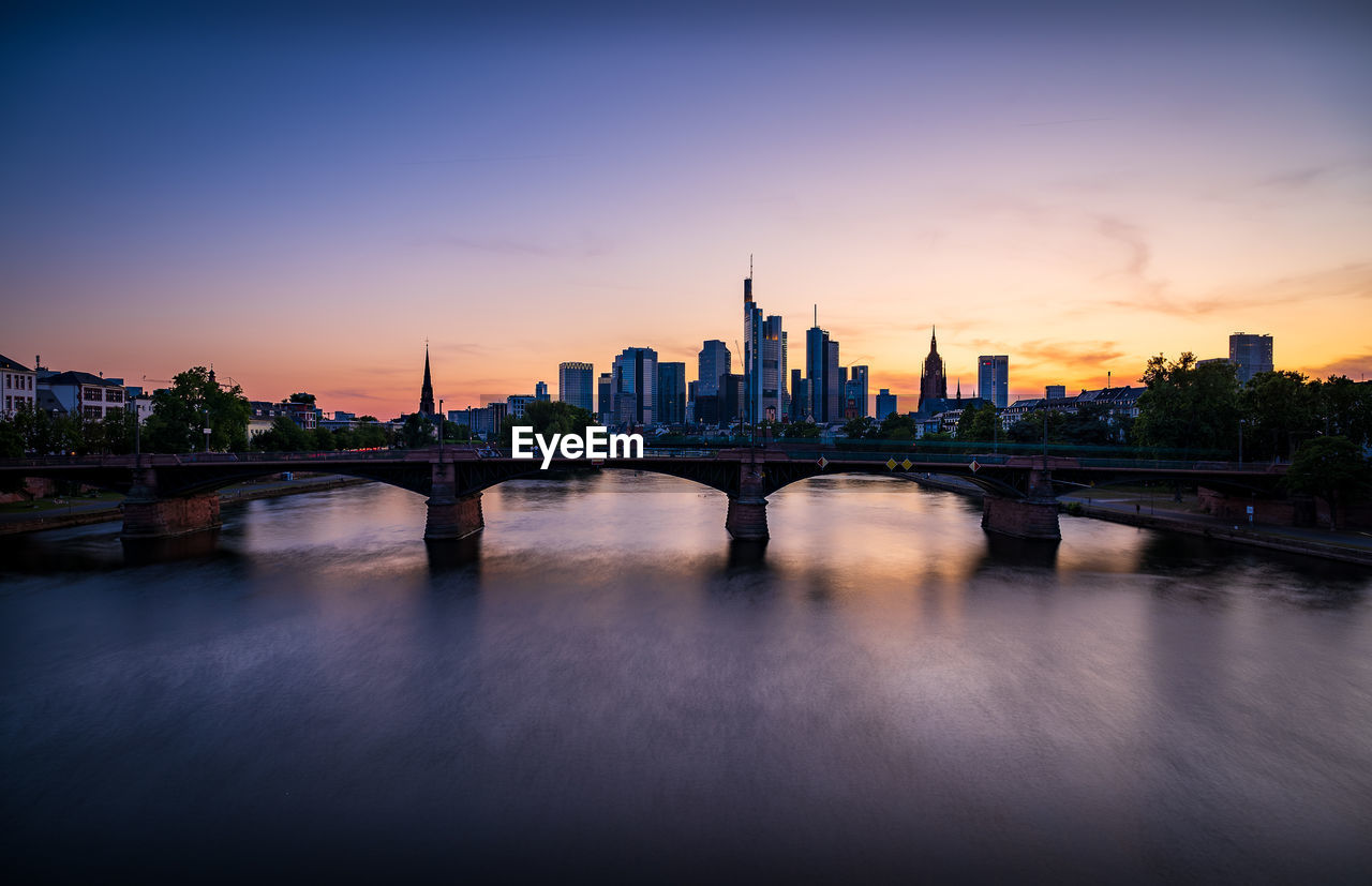 Bridge over river in city against sky during sunset