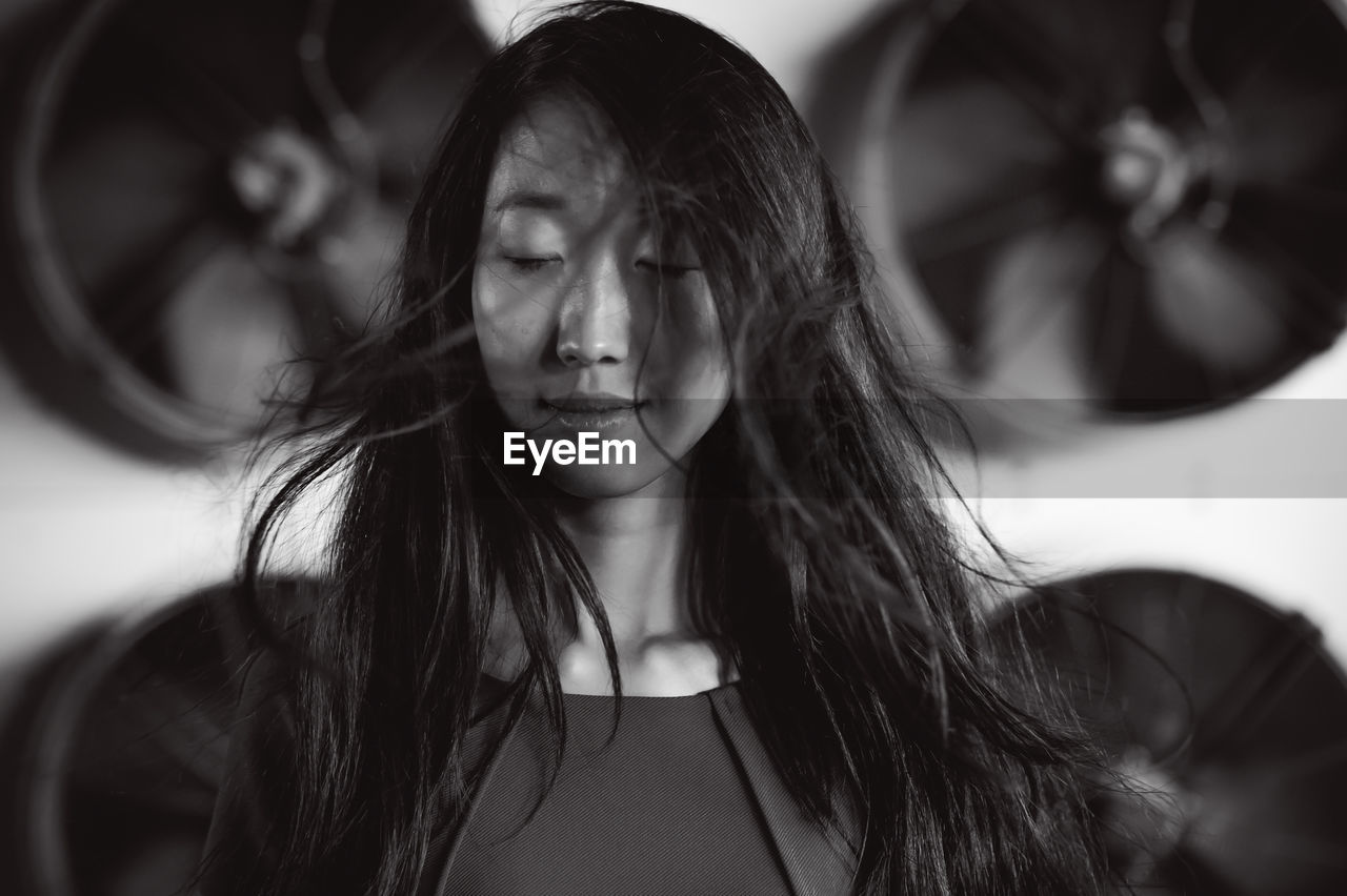 Young woman with tousled hair standing against exhaust fans