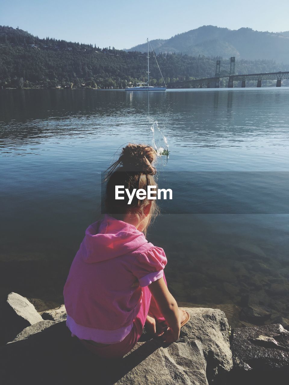 Girl sitting on rock by lake during sunny day