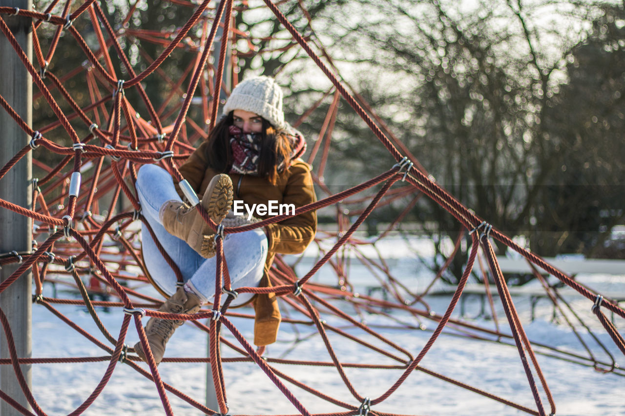 Full length portrait of woman resting on ropes at snow covered park