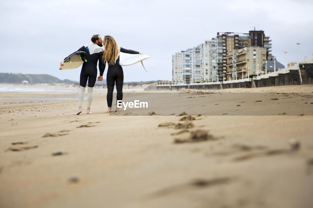 Couple kissing while holding surfboards at beach