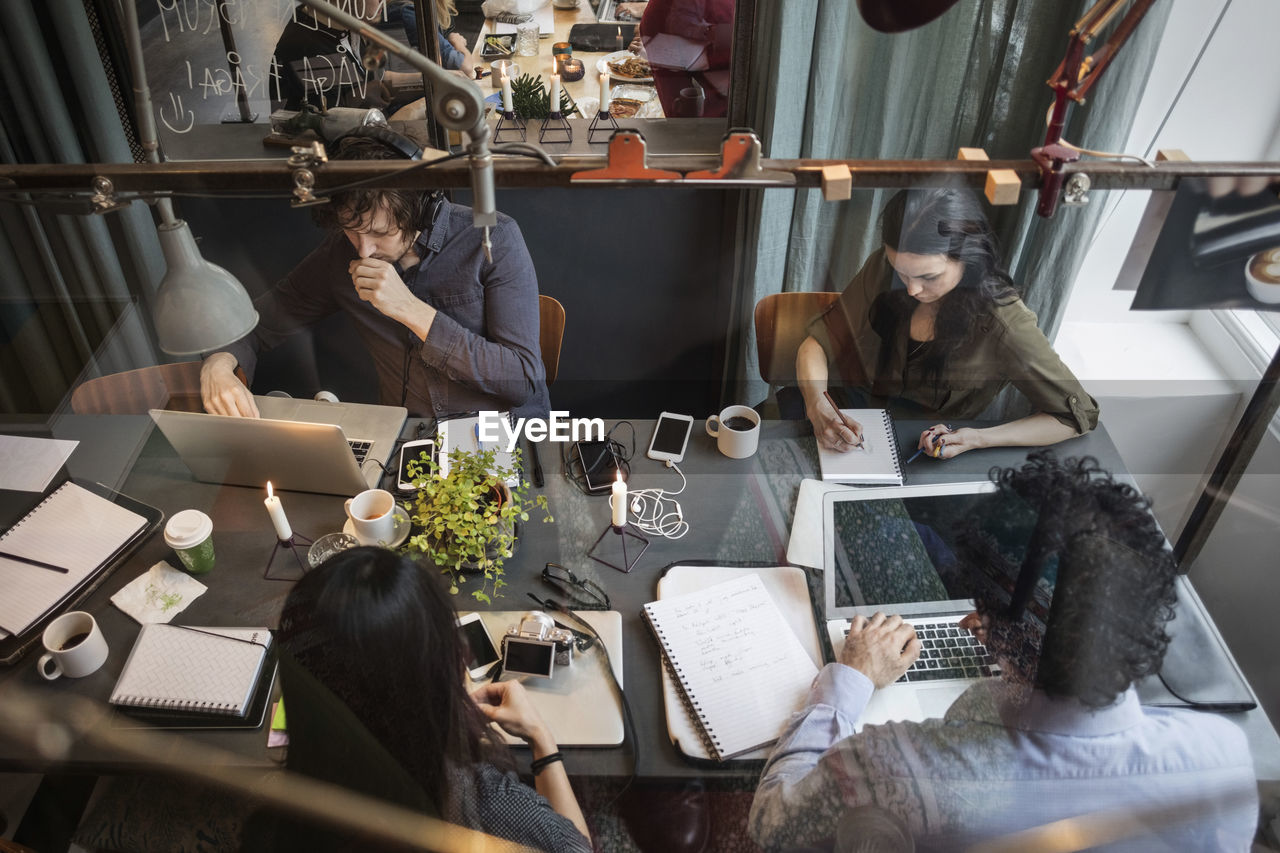 High angle view of creative team working at table in office seen through glass