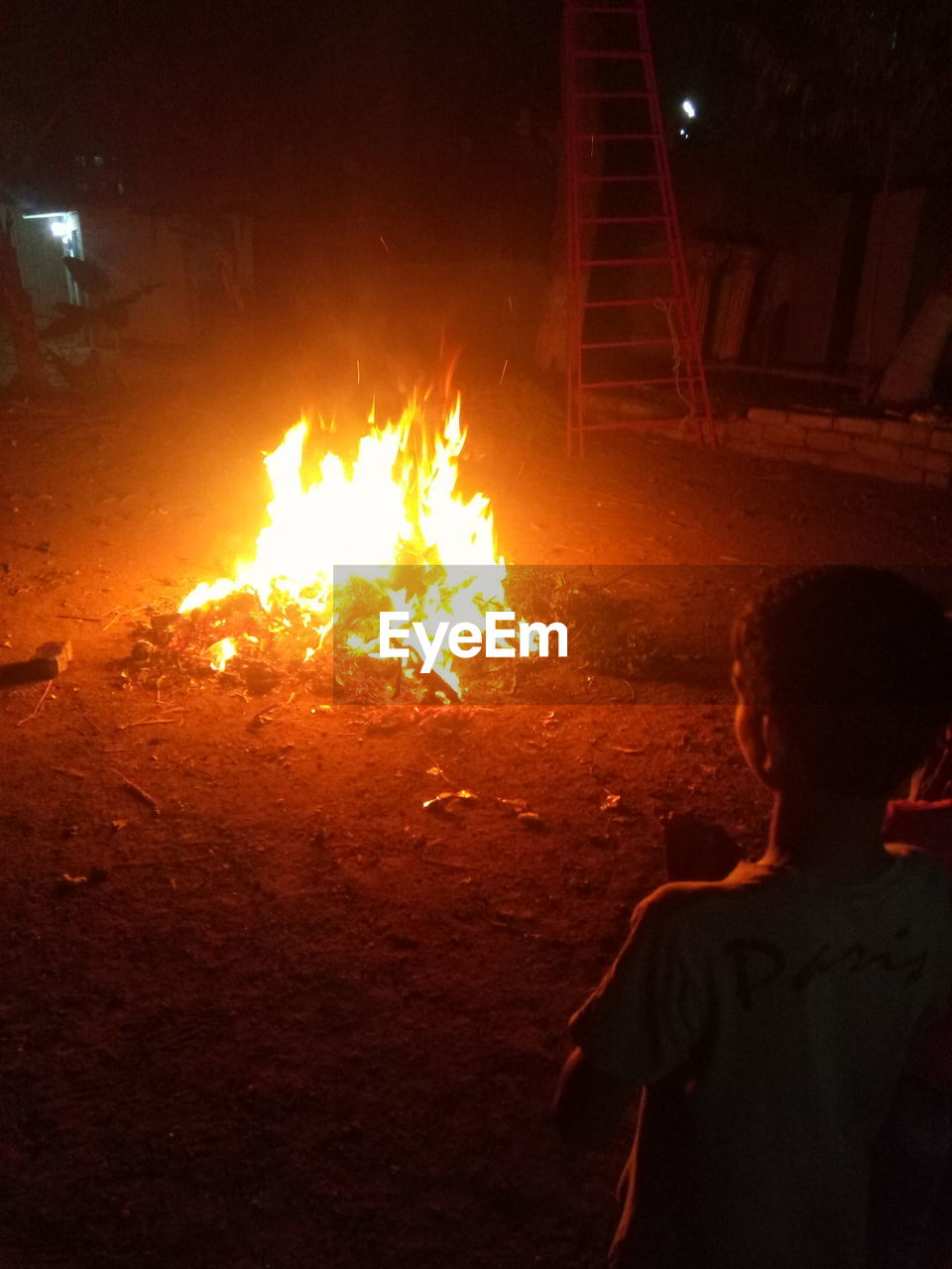 Rear view of boy standing by illuminated campfire at night