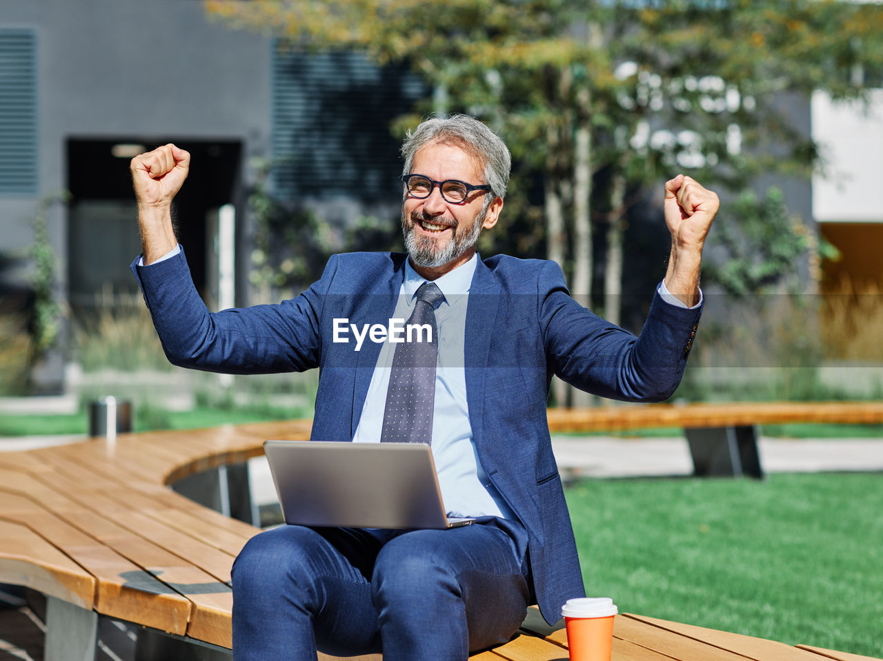 Happy businessman sitting with laptop outdoors on sunny day