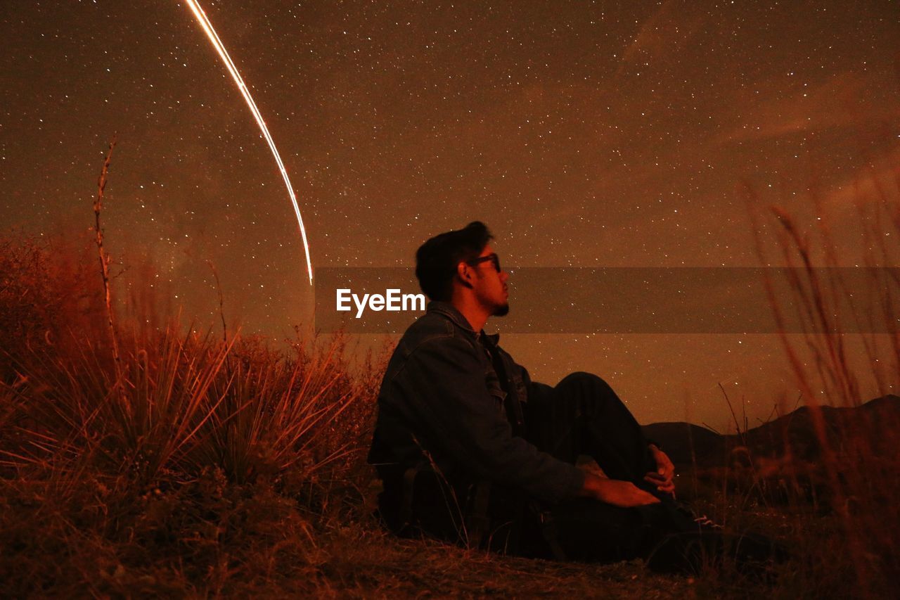 Side view of man sitting against sky at night