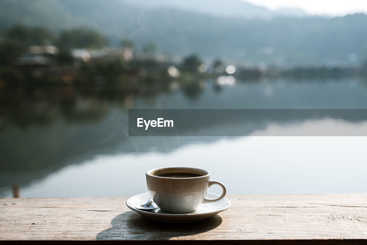 A cup of coffee on a rustic wooden table with village blurred background.