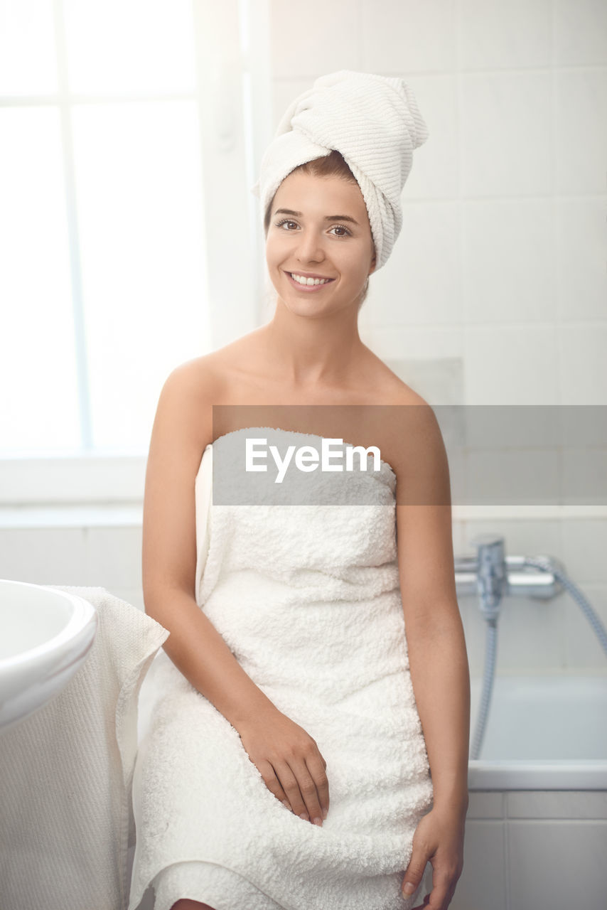 Portrait of smiling young woman sitting on bathtub at home