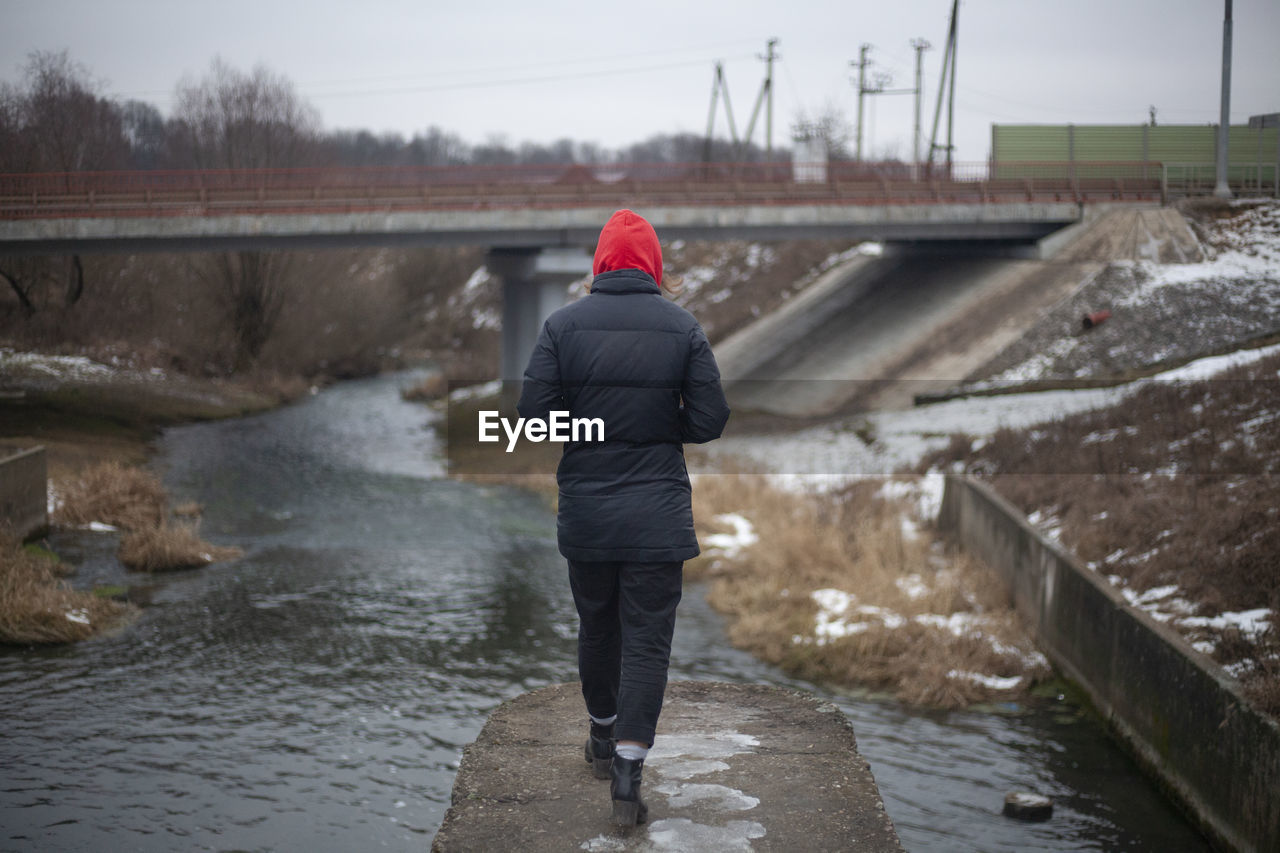 FULL LENGTH REAR VIEW OF WOMAN STANDING IN CANAL DURING WINTER