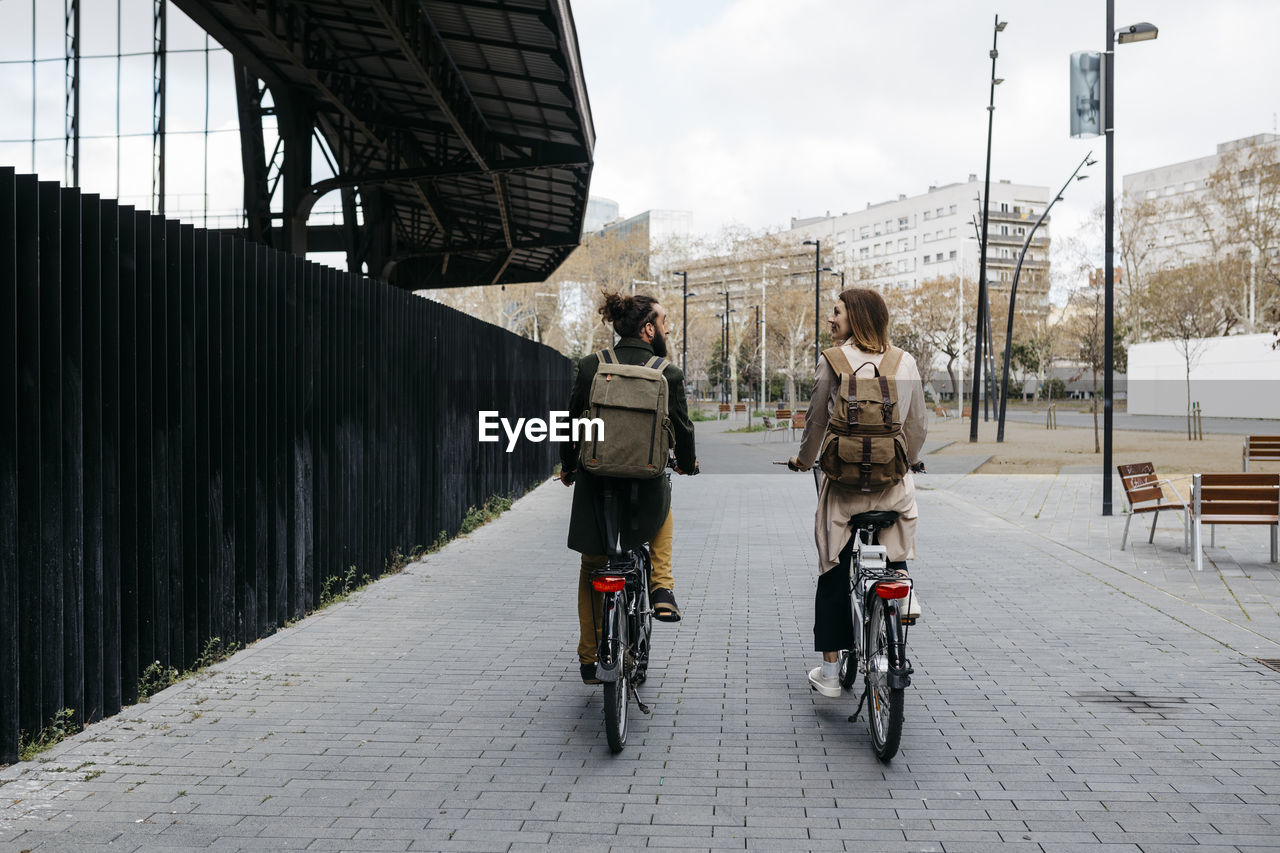 Rear view of couple riding e-bikes in the city talking to each other