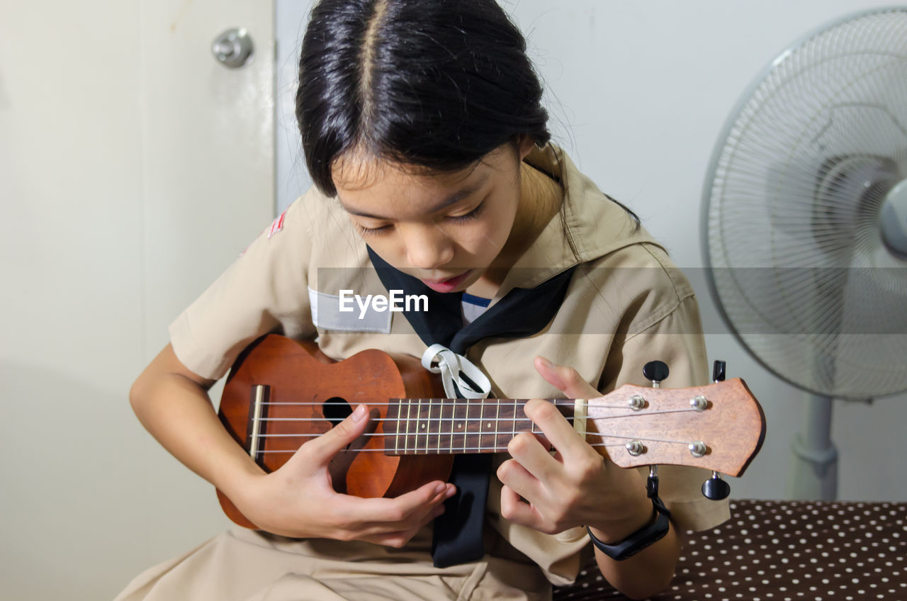 Girl playing small guitar while sitting at home