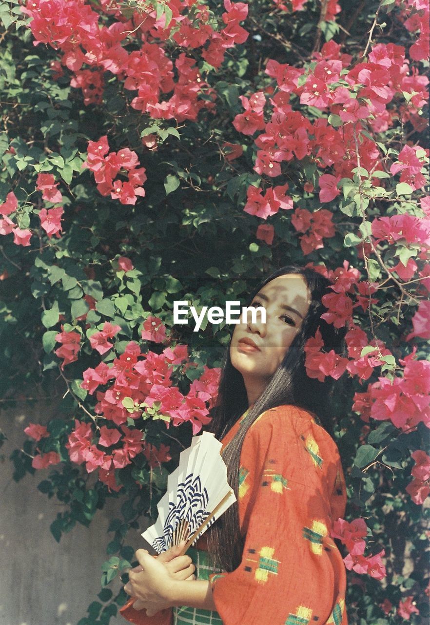 PORTRAIT OF SMILING YOUNG WOMAN HOLDING FLOWERING PLANT