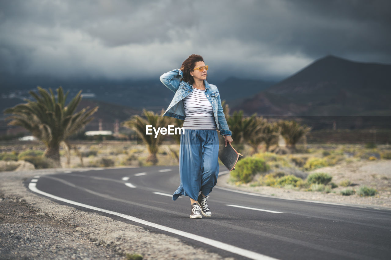 Full length of woman walking on road against cloudy sky