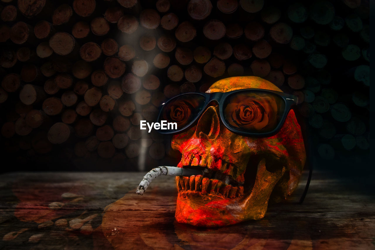 Close-up of human skull with cigarette and sunglasses on table