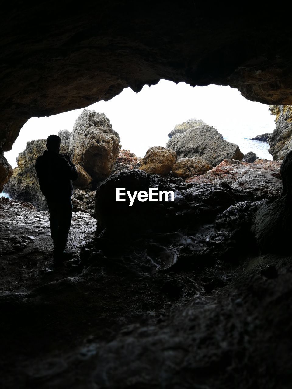 REAR VIEW OF MAN STANDING ON ROCK CAVE