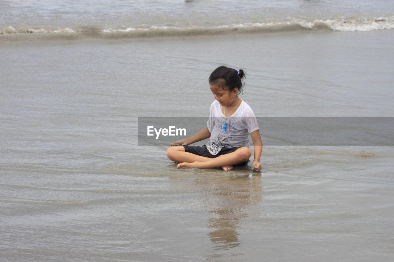 Rear view of a girl sitting on sand of beach.