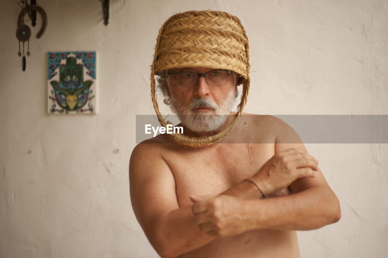 Shirtless senior man wearing wicker basket at home