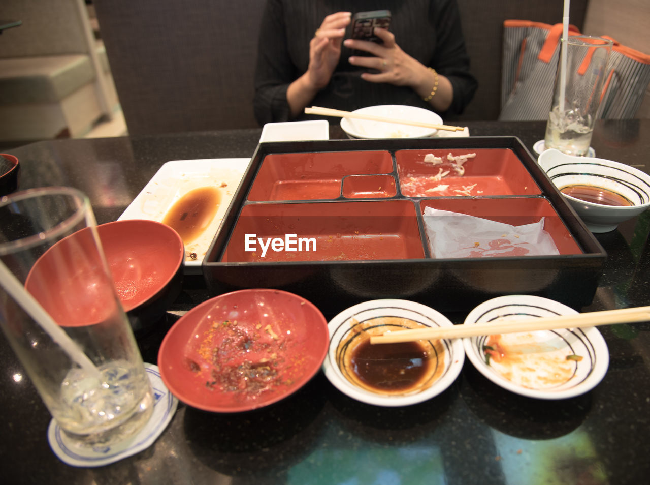 Midsection of woman using mobile phone by empty containers on table