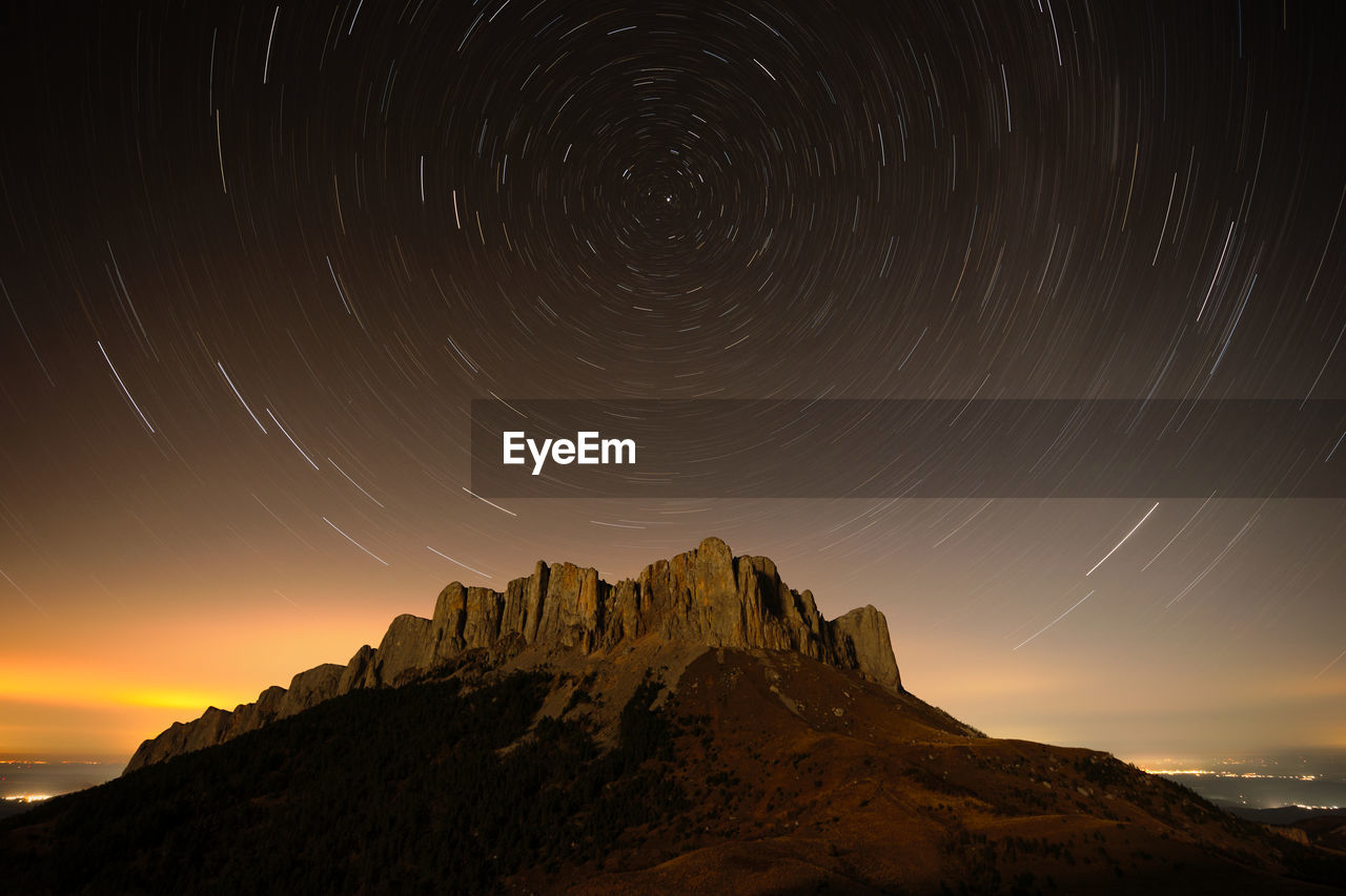 Twilight panoramic mountain view, starry sky and clouds, city lights in the background