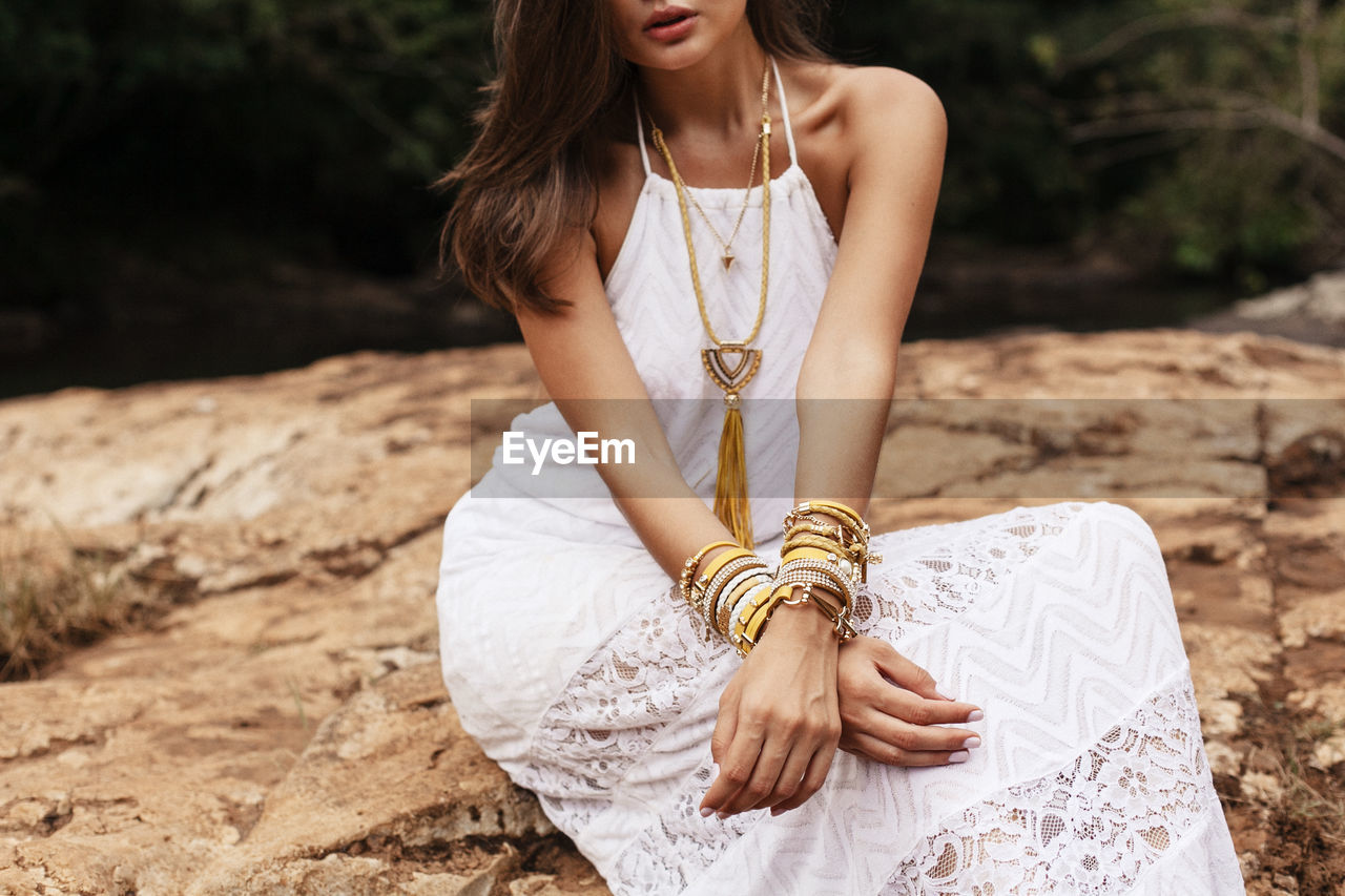 Young woman wearing dress sitting on rock formation at forest