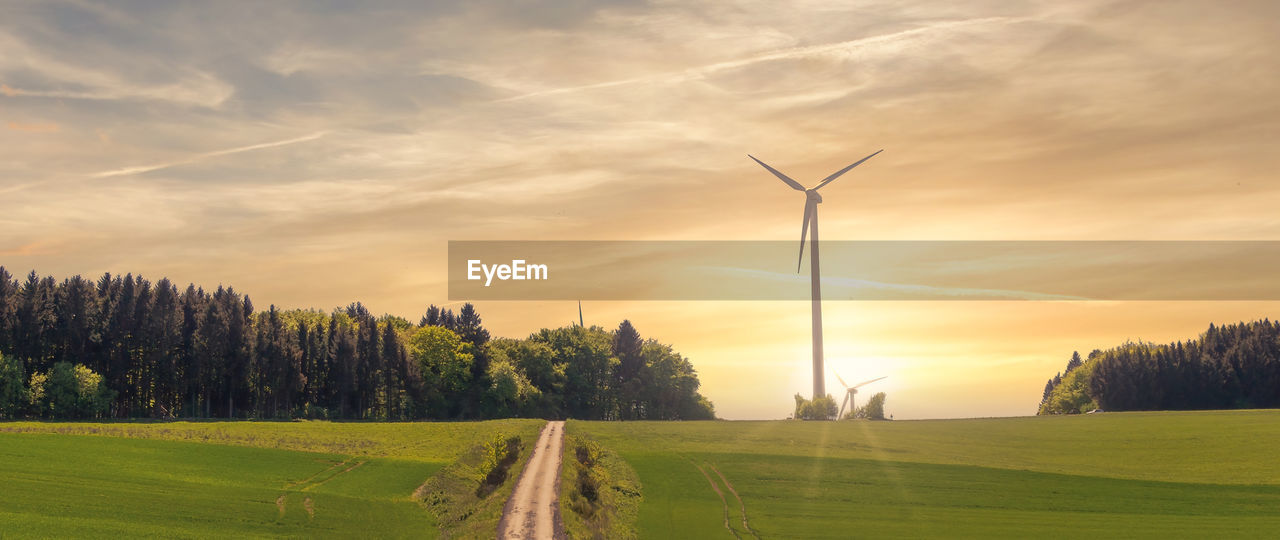 Scenic view of field and wind turbines against sky during sunset