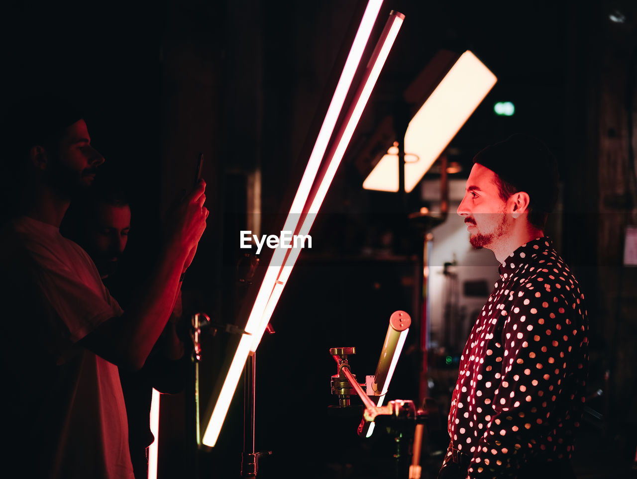 YOUNG MAN STANDING BY ILLUMINATED LIGHTS