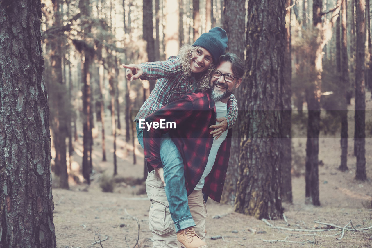 Smiling man carrying woman on back against tree